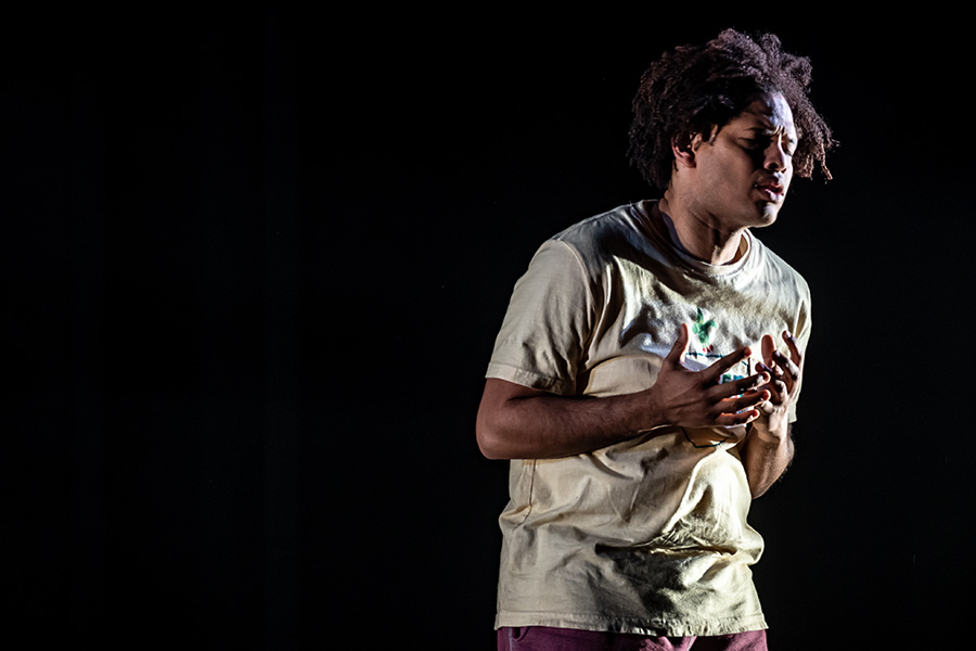 Photo of actor Brandon Michael Arrington performing on stage, the background is a deep black, with the actor in the spotlight.