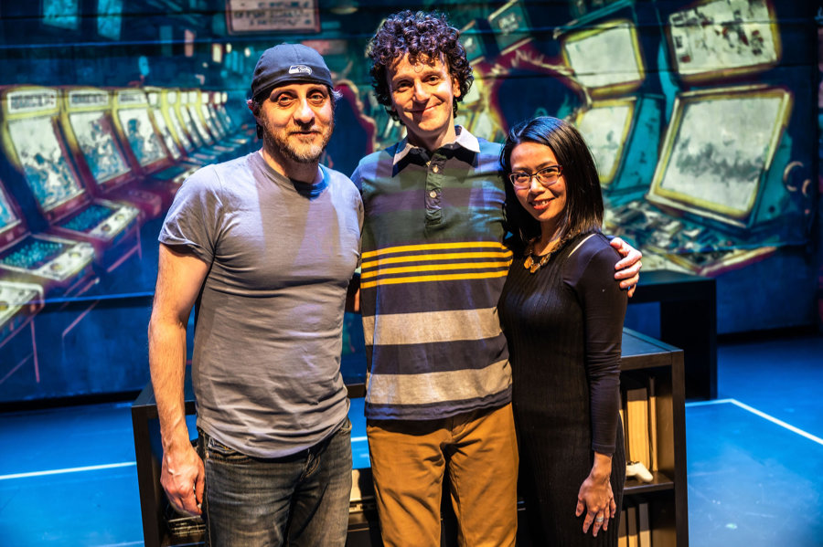 Photo of Director Haysam Kadri, actor Nabil Traboulsi, and writer Winnie Yeung, posing together in front of a projected backdrop on the set of Homes: A Refugee Story.