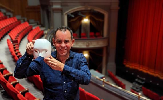 Dennis Garnhum stands in the balcony level of the Spriet Stage at the Grand Theatre, holding a mask from the play Phantom of the Opera.