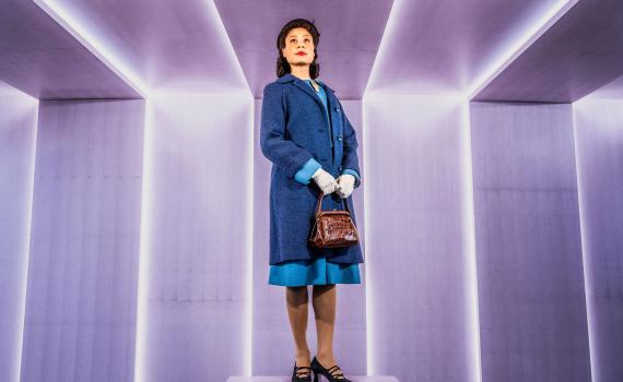 Beck Lloyd in character as Viola Desmond, stands in front of a light purple wall with vertical strips of light that continue along the ceiling.