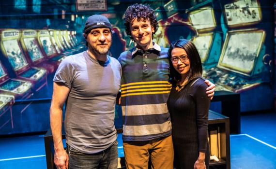 Director Haysam Kadri, actor Nabil Traboulsi, and writer Winnie Yeung pose together in front of a projected backdrop on the set of Homes: A Refugee Story