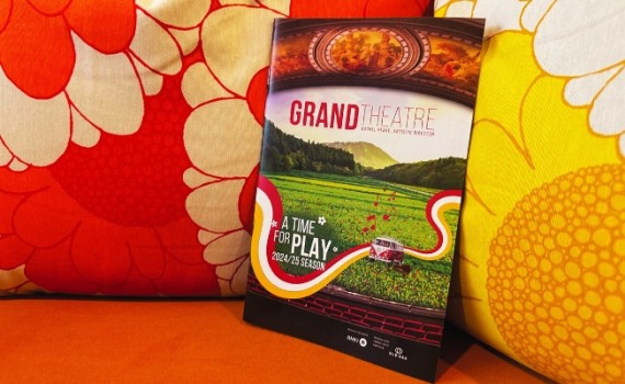 A copy of the Grand Theatre's 2024-25 Season brochure positioned against colourful floral cushions.