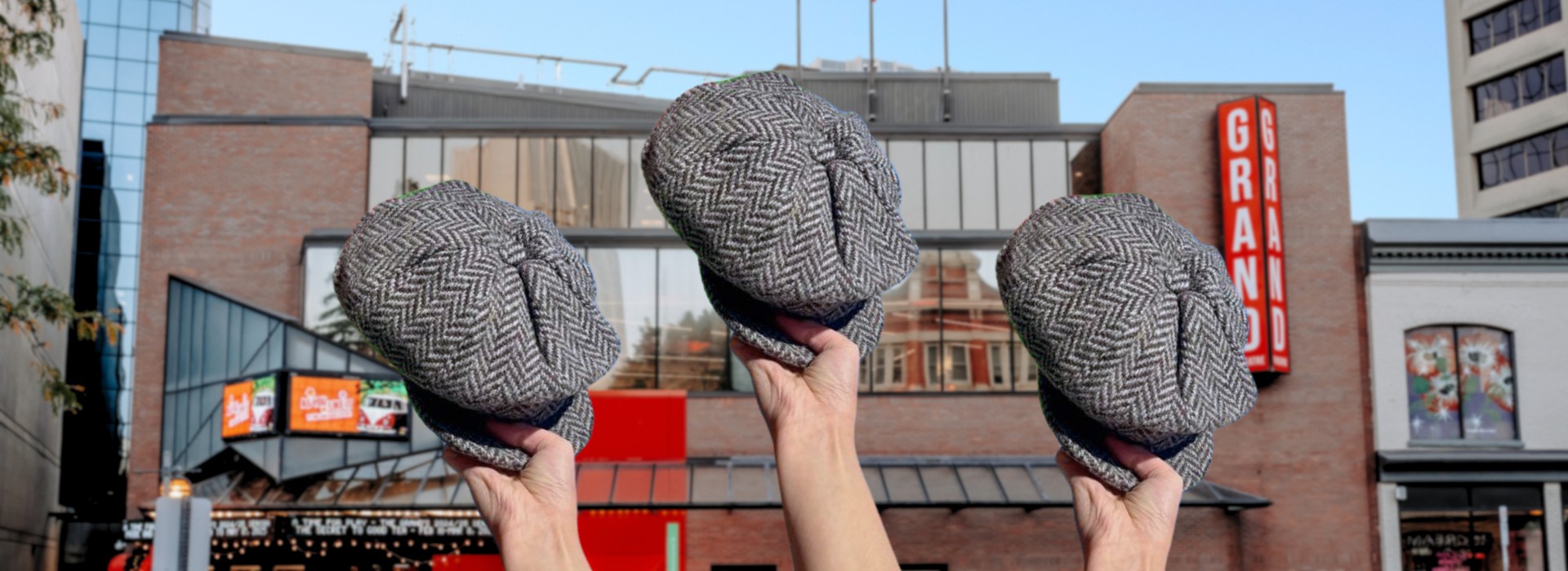 Three newsboy caps are held up in the foreground, the Grand Theatre visible in the background.