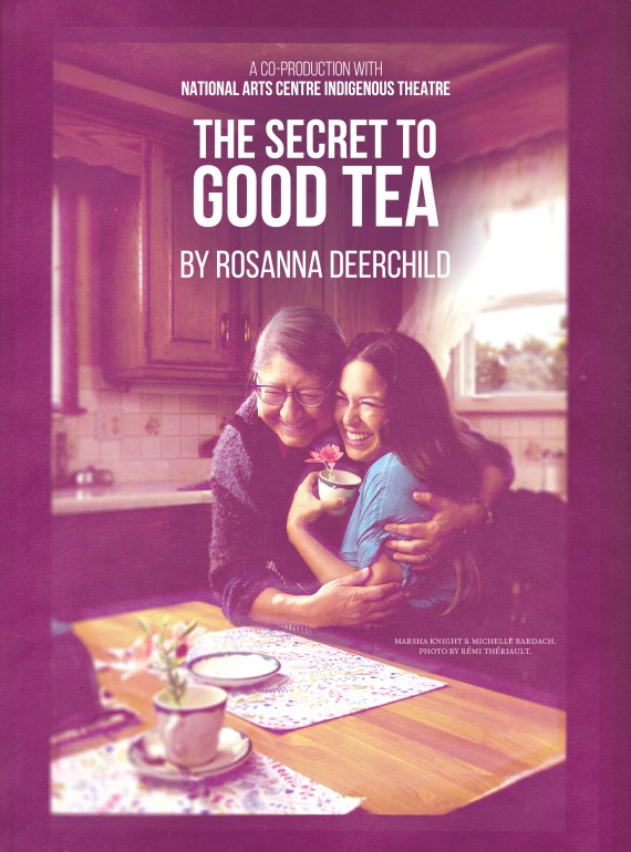 An older woman hugs a younger woman seated at a kitchen table as they enjoy a cup of tea.